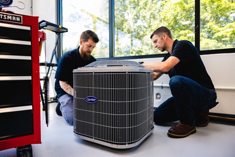 Two trainees working on a Carrier air conditioner unit inside the SEER Institute facility